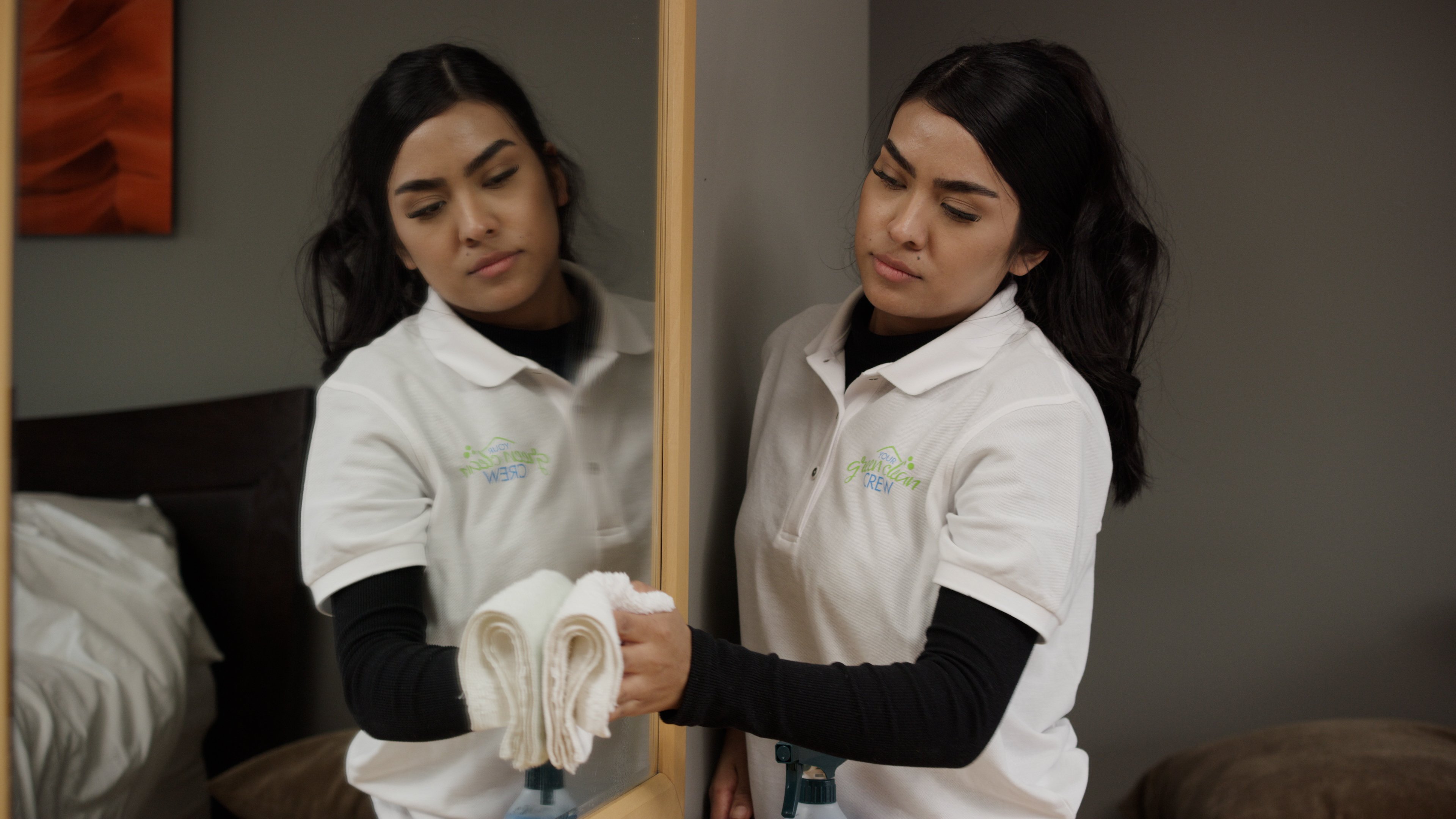 Woman cleans bedroom mirror with cloth